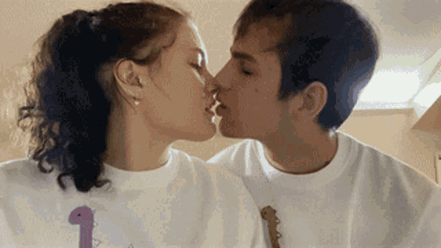 a man and a woman are kissing and the woman is wearing a white shirt with a dinosaur on it