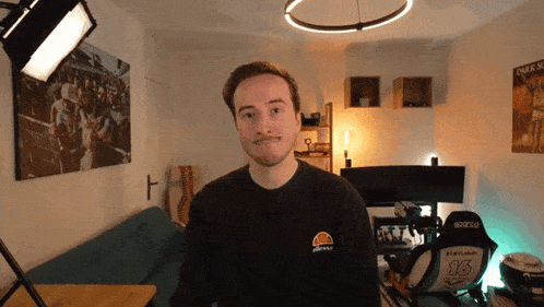 a man wearing a black ellesse sweatshirt stands in front of a couch