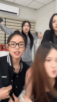 a group of young women are standing next to each other in a room with an air conditioner .