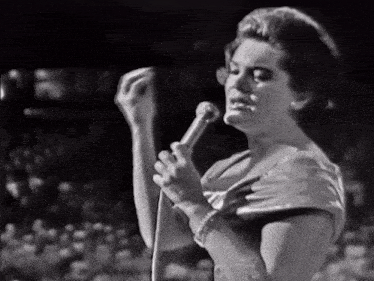 a woman singing into a microphone with a crowd behind her
