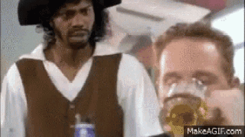 a man in a pirate costume is holding a glass of beer next to another man in a white shirt .