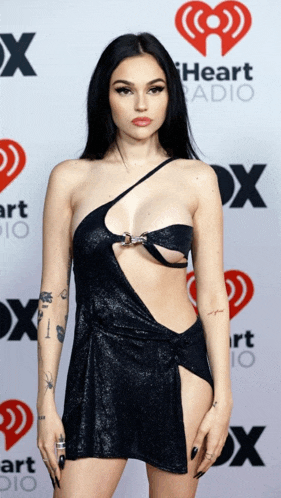 a woman in a black dress is standing in front of a heart radio sign