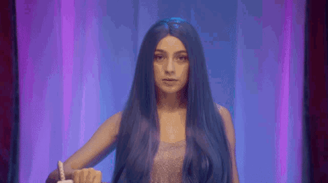 a woman with long blue hair is holding a remote control