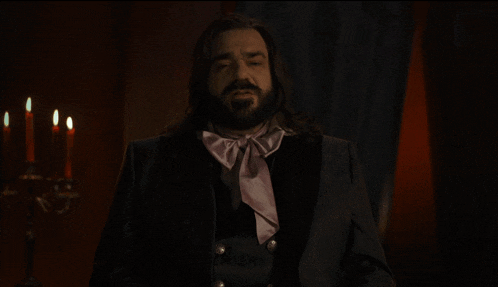 a man with long hair and a beard is standing in a dark room with candles