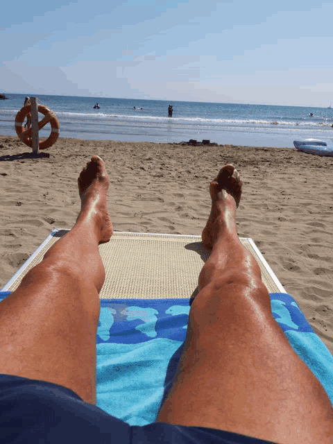 a person laying on a beach with their feet up and a life preserver in the background