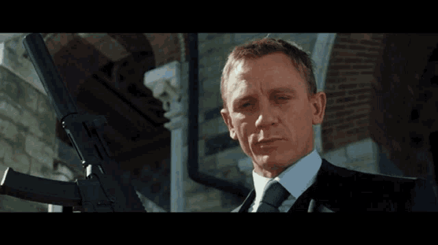 a man in a suit and tie is holding a gun in front of a building