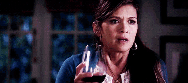 a woman in a blue sweater is holding a glass of wine .