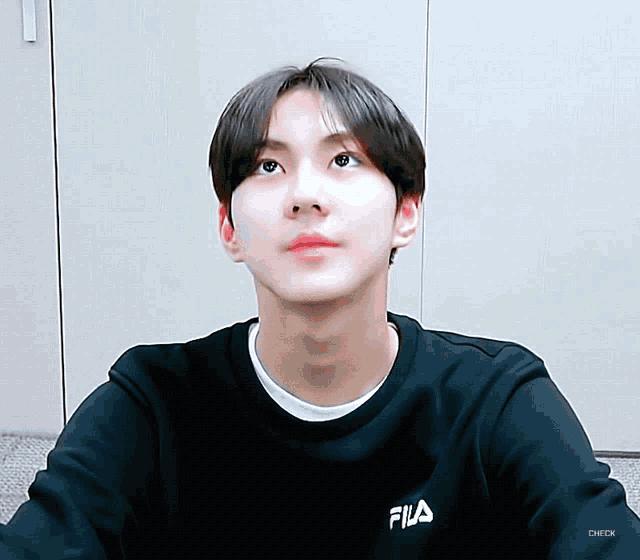 a young man wearing a black fila sweatshirt looks up at the sky