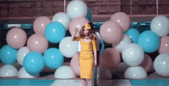 a woman in a yellow dress is standing in front of a wall of pink and blue balloons