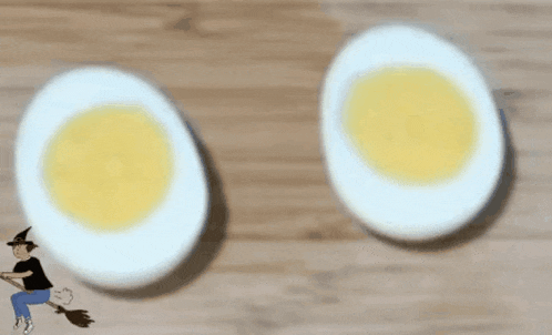 two hard boiled eggs on a table with a witch on a broom in the background