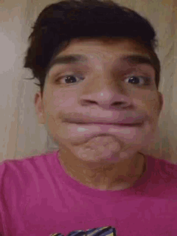 a young man wearing a pink shirt is making a face