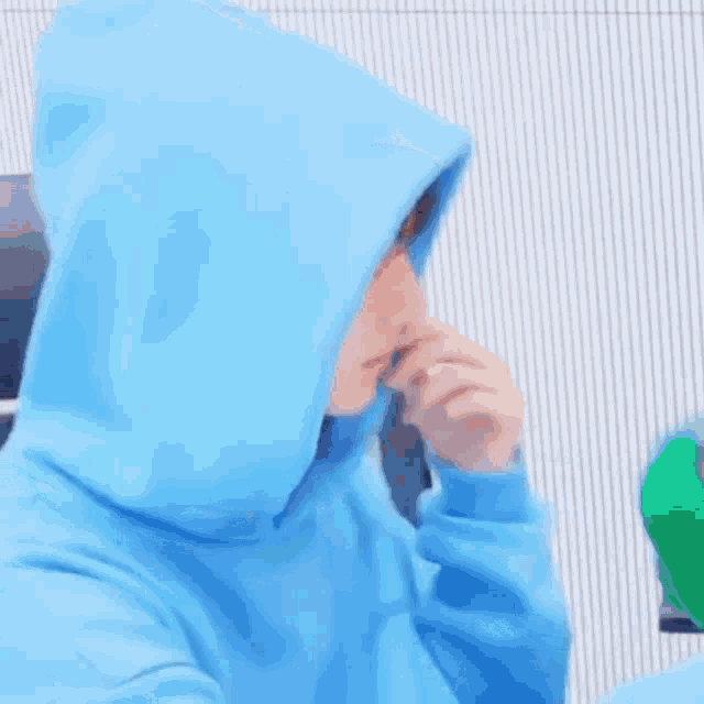 a young man wearing a blue hoodie is sitting in front of a white wall .