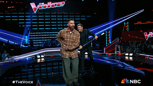 a man in a plaid shirt is dancing on a stage in front of a nbc sign