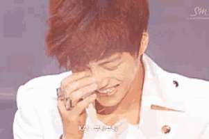a young man with red hair is covering his face with his hand and smiling .