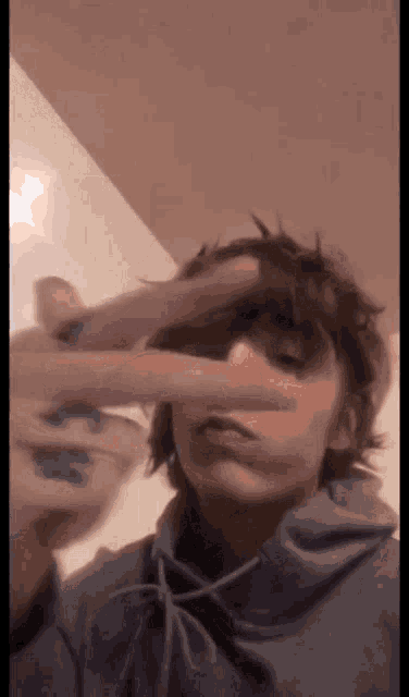 a young man in a blue hoodie is covering his face with his hands .