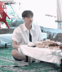 a man is sitting on the floor in front of a table with plates of food on it .