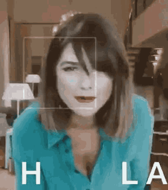 a woman in a blue shirt is standing in a living room with the word hola written on the bottom .