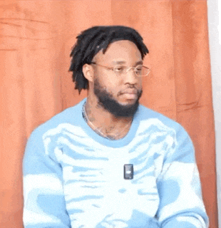 a man wearing glasses and a blue sweater with a skeleton on it is sitting in front of a curtain .