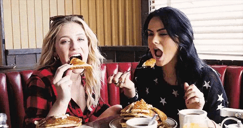 two women are eating pancakes together in a diner .