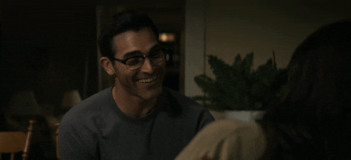 a man wearing glasses and a grey shirt smiles at a woman