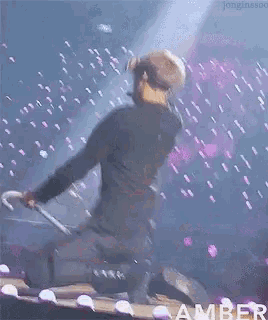 a man is kneeling down on a stage holding a microphone and the word amber is on the bottom