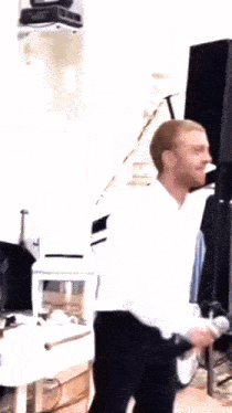 a man in a white shirt and black pants is standing in a room with a microphone in his hand .