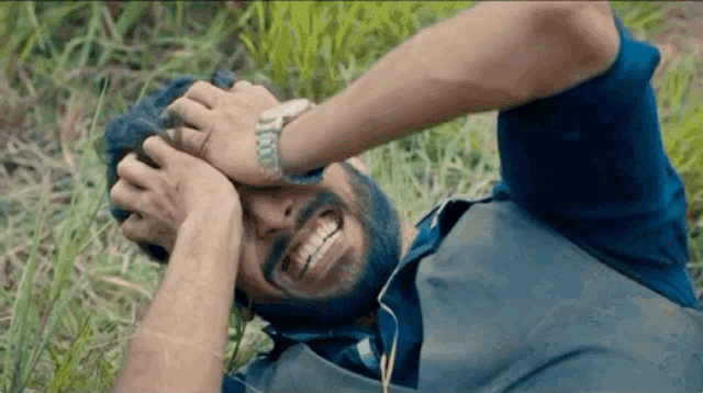 a man with a beard is laying in the grass with his hands on his head .