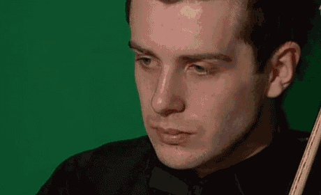 a man in a black shirt and bow tie is holding a cue in front of a green background .