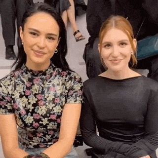 two women are sitting next to each other in a crowd and smiling .