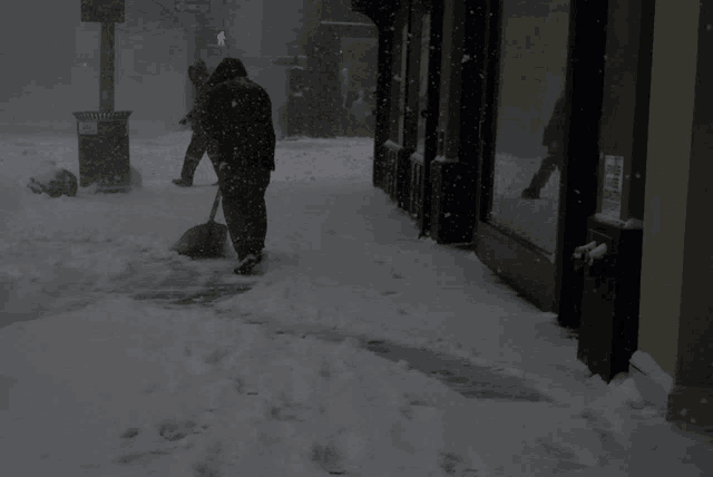 a man is shoveling snow on a sidewalk in front of a store that has a sign that says " no dogs "