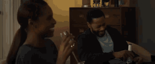 a man and a woman are sitting on a couch laughing and drinking .