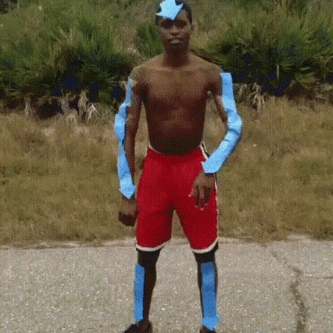 a shirtless man wearing red shorts and blue sleeves is standing on a sidewalk .