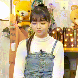 a girl in a denim dress and a white shirt is standing in front of a teddy bear .