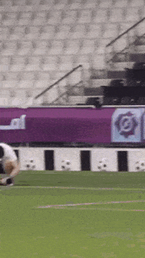 a man is kneeling on a soccer field in front of a stadium with empty seats .