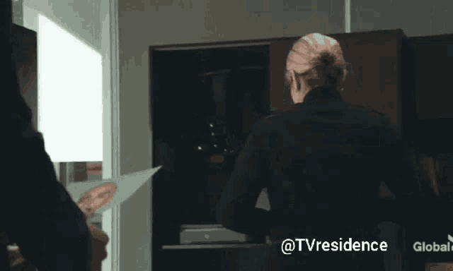 a woman in a black jacket is standing in front of a tv with the words @tvresidence on the bottom right