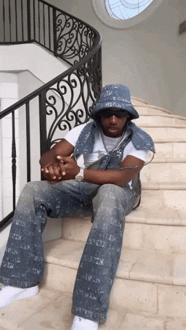 a man is sitting on a set of stairs wearing a denim vest and a bucket hat