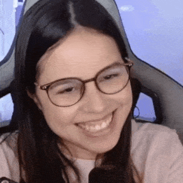 a woman wearing glasses is smiling in front of a microphone while sitting in a chair .