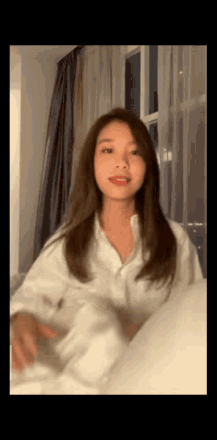 a woman in a white shirt is sitting on a bed and holding a white pillow .