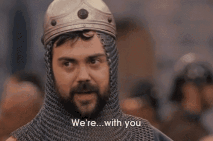 a man with a beard wearing a helmet and chain mail is talking to someone .