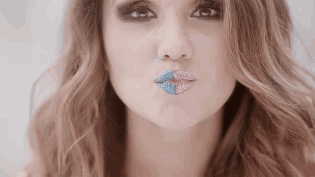 a close up of a woman blowing a kiss with her lips painted blue and pink