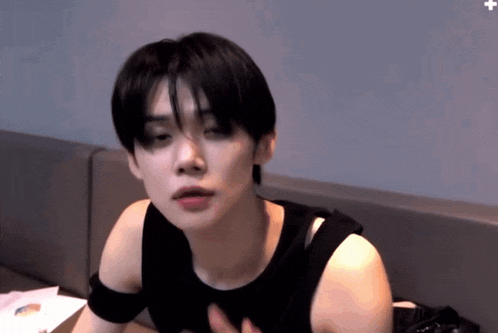 a young man wearing a black tank top is sitting on a couch .