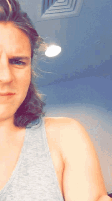 a man with long hair is wearing a grey tank top and taking a selfie