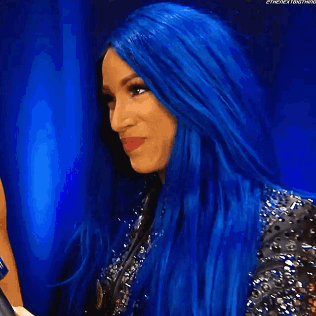 a woman with blue hair and pink lipstick is wearing a spiked jacket .