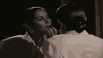 a woman is looking at herself in a mirror and applying lipstick .