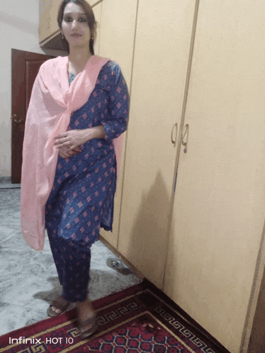 a woman wearing a blue dress and a pink scarf is standing in front of a infinix hot 10 phone