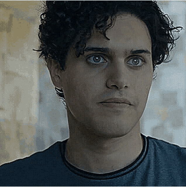 a close up of a man 's face with curly hair wearing a blue shirt and looking at the camera .