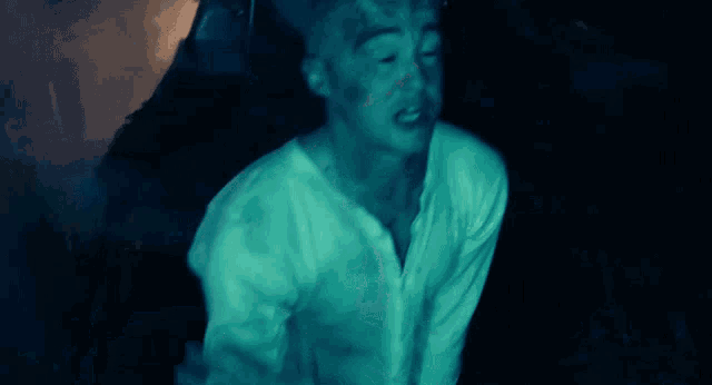 a man in a white shirt is sitting in a dark room with a blue light behind him