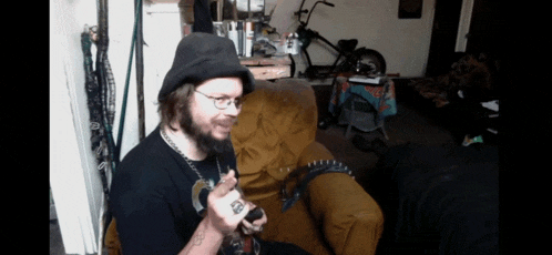 a man with a beard wearing a hat and glasses is sitting in a chair