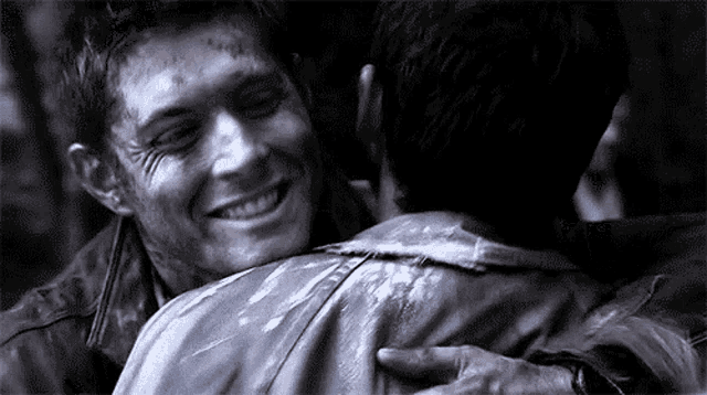 a man is hugging another man in a black and white photo and smiling .