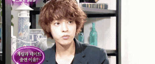 a man with curly hair is standing in front of a shelf with bottles on it .